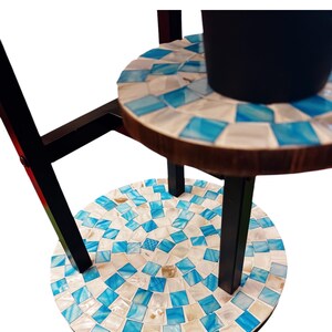 May include: A three-tiered plant stand with a black metal frame and round, mosaic-tiled shelves. The shelves are made of wood and have a blue and white mosaic pattern.