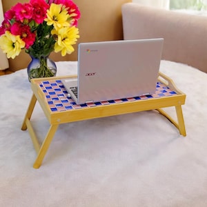 May include: A bamboo laptop tray with a blue and pink checkered tile design. The tray is folded up and has a laptop on top of it. The laptop is closed and has the word "acer" on the back.