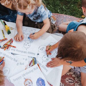 K&ouml;nnte beinhalten: Drei Kinder f&auml;rben personalisierte Geburtstagskarten mit Buntstiften aus. Die Karten zeigen eine Comiczeichnung eines Kindes mit einem Ballon und dem Text "happy birthday ila!"