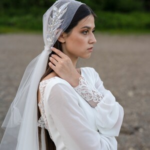 May include: A bride wearing a white wedding dress with lace detailing on the sleeves and back. She is wearing a veil with a jeweled headpiece.