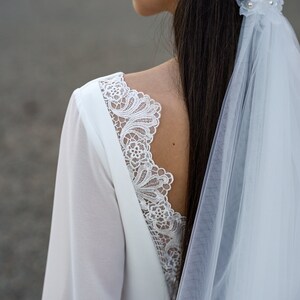 May include: A white wedding dress with long sleeves and a lace back detail. The dress is paired with a white veil.