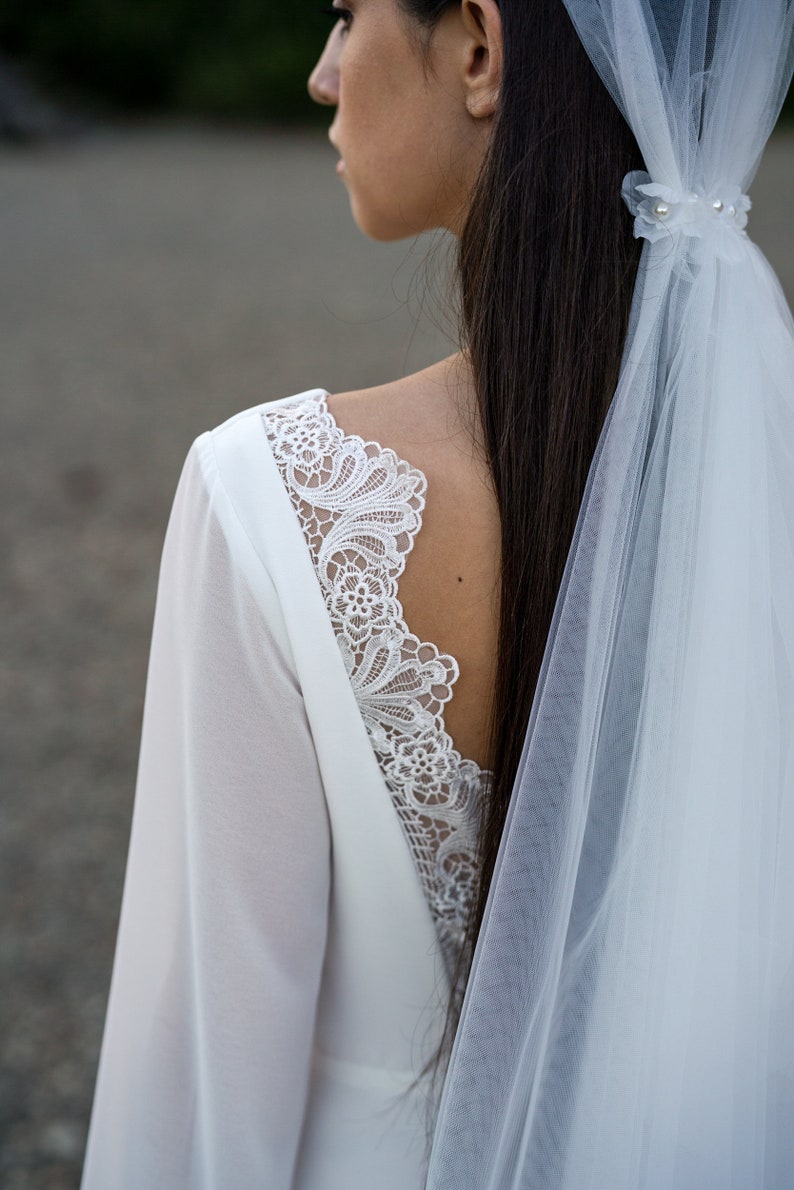 May include: A white wedding dress with long sleeves and a lace back detail. The dress is paired with a white veil.