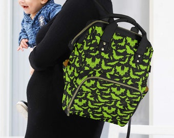 May include: Black and green backpack featuring a bat design. The bag has a top handle and several pockets. A person wearing a black dress is carrying the backpack.