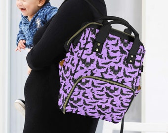 May include: A purple and black bat-patterned nappy bag backpack. The bag has a top handle, multiple pockets, and adjustable straps. The bag is being carried by a person wearing a black dress.