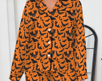 May include: Orange pajama set with a black bat pattern. The long-sleeved top has a button-down front and black trim. The matching pants have a relaxed fit. The pajamas are made of a soft, lightweight fabric, perfect for Halloween.