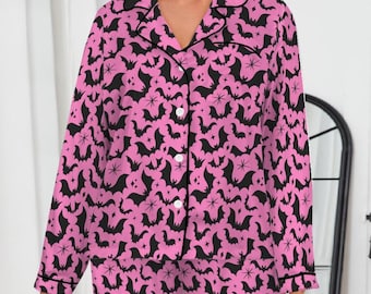 May include: Pink pajama set with a black bat pattern. The set includes a button-down shirt with a notched collar and long sleeves, and matching pants. The pajamas have black trim and are made of a soft, comfortable material.