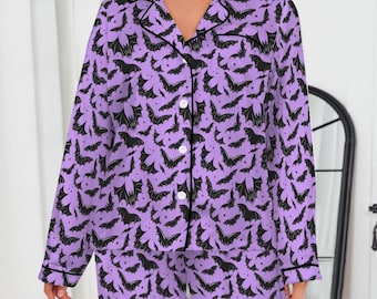 May include: Lavender pajama set with a black bat pattern. The set includes a button-down shirt with a notched collar and long sleeves, and matching pants. The edges of the shirt and pants are trimmed with black piping. The pajamas are made of a soft, comfortable material.