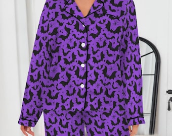 May include: Purple pajama set with a black bat and spider pattern. The long-sleeved top has a collared neckline and button-down front. The pants are long and straight-legged. The set is trimmed with black piping.