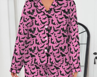 May include: Pink pajama set with a black bat pattern. The long-sleeved top has a button-down front and a notched collar. The pants are long and straight-legged. The set is trimmed with black piping.