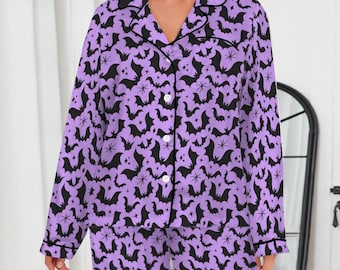 May include: A two-piece pajama set in a light purple color, covered in a black bat pattern. The set includes a button-down shirt with black trim and matching pants. The pajamas are made of a soft, comfortable material.