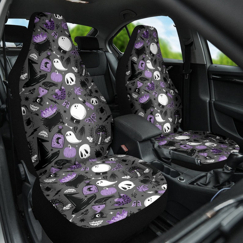 May include: Car seat covers with a Halloween-themed pattern. The design features a repeating pattern of witch hats, cauldrons, ghosts, skulls, pumpkins, and other spooky elements in black, white, and purple on a gray background.