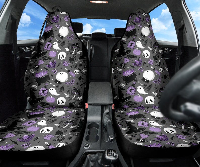 May include: Two car seat covers with a Halloween-themed pattern. The design features white ghosts, skulls, cauldrons, witch hats, and pumpkins on a gray background, with purple accents. The seats are designed to fit most car models.