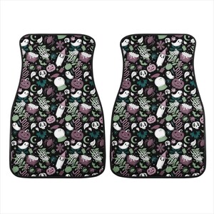 May include: Two black car floor mats with a Halloween themed pattern. The pattern features ghosts, pumpkins, cauldrons, and other spooky elements in shades of green, purple, and white on a black background.
