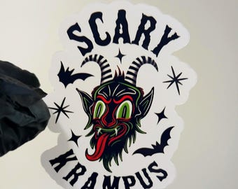 May include: A white sticker with a black and green Krampus illustration. The sticker features the text "SCARY KRAMPUS" in a stylized font, with bats and stars around the image.