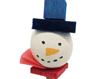 May include: A snowman ornament crafted from a white spherical head with a painted orange carrot nose and black dot eyes and mouth. It wears a blue wooden top hat, a red wooden base, and a pleated pink paper collar, suspended by a brown cord.