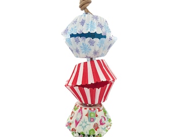 May include: A string of three cupcake liners, each with a different festive pattern. The top liner is blue and white with snowflakes, the middle liner is red and white striped, and the bottom liner is green, white, and red with a Christmas tree design.