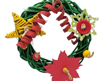 May include: A green woven wreath ornament decorated with a yellow woven star, a red spiral ribbon, a green and white snowflake cutout with a red button center, a red paper poinsettia, and small red and yellow wooden beads on twine.