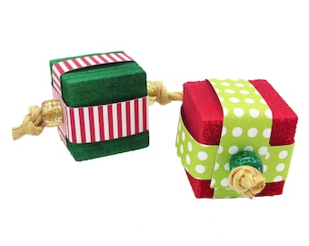 May include: Two small, wrapped gift boxes connected by a string. The box on the left is green with red and white stripes. The box on the right is red with green polka dots.