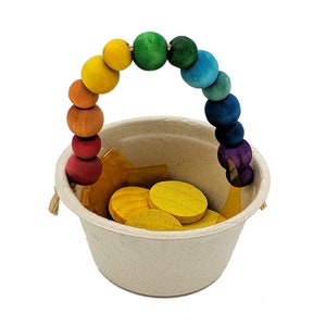 May include: A small, beige paper pot filled with yellow wooden coins and gold-colored paper. A rainbow-colored wooden beaded handle arches over the pot. The beads transition from red to purple.
