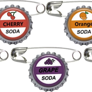 May include: Five metal bottle cap pins featuring colorful fruit illustrations and text. Each cap displays a specific flavor: Cherry, Orange, Lemon Lime, Grape, and Pineapple, with the word SODA printed below each fruit graphic on a white background.