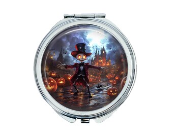 May include: A silver compact mirror with a Halloween themed design. The image features a skeleton wearing a top hat and a red and black costume, standing in front of a spooky castle with pumpkins scattered around.