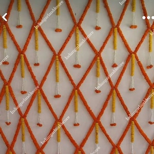 Pode incluir: Uma parede decorada com guirlandas de flores laranja e amarelas em forma de losango. As guirlandas são feitas de flores de calêndula e são enfiadas com fio branco. O texto "indiangarlanddecor" aparece várias vezes na imagem.