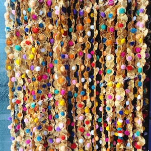 Puede incluir: Primer plano de una guirnalda colorida hecha de círculos metálicos dorados y pompones. La guirnalda está hecha de múltiples hebras y es perfecta para agregar un toque festivo a cualquier ocasión.