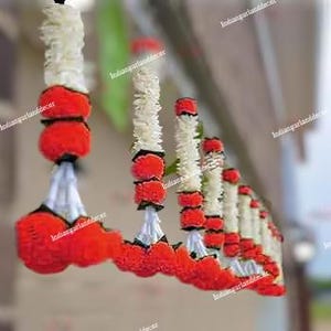 May include: A string of red and white floral garlands, hanging from a ceiling or doorway. The garlands are made of small, round flowers and are tied together with white string.