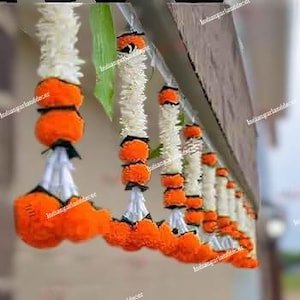 May include: A garland of orange and white marigold flower strings hanging from a wooden beam.