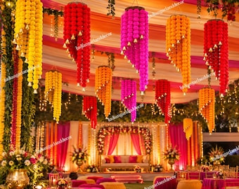 May include: Multiple hanging floral garlands in yellow, red, orange, and magenta, each featuring small gold bells attached at intervals. These decorative strings are suspended from a ceiling draped with colorful fabric in a festive setting.