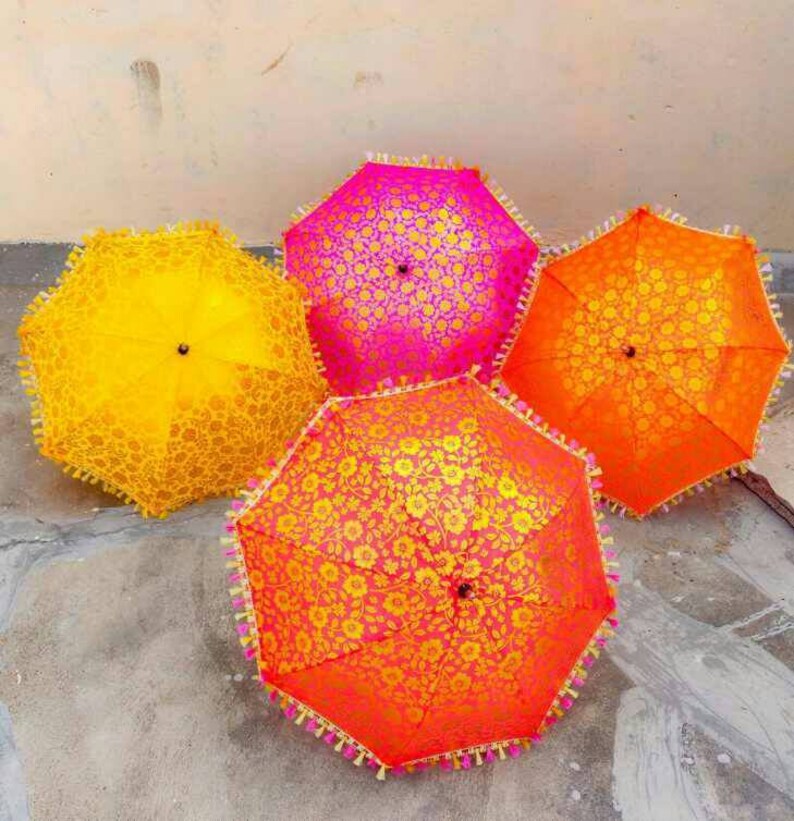 May include: Four decorative umbrellas with floral patterns. Two umbrellas are yellow, one is pink, and one is orange. The umbrellas have tassels around the edges.