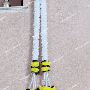 May include: Two white flower garlands with yellow flower accents. The garlands are hanging from a wall.