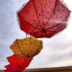 May include: Four colorful umbrellas with floral patterns hang from the ceiling. The umbrellas are red, pink, yellow, and orange.