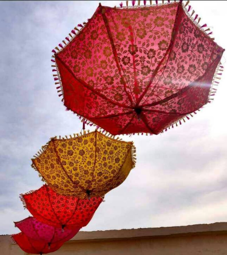 May include: Four colorful umbrellas with floral patterns hang from the ceiling. The umbrellas are red, pink, yellow, and orange.