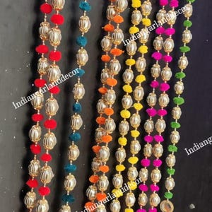 Puede incluir: Un conjunto de seis guirnaldas decorativas para colgar en la puerta con cuentas plateadas y pompones de colores. Cada guirnalda tiene un espejo y un borla en la parte inferior. Los colores de los pompones son rojo, azul verdoso, naranja, amarillo, rosa y verde.