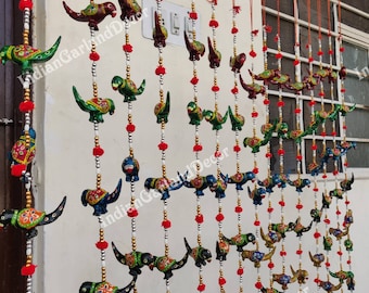 May include: A colorful string of wooden bird ornaments, painted in various shades of green, blue, red, and gold, with red pom-poms interspersed throughout. The birds are strung on silver and gold chains, creating a decorative hanging garland.
