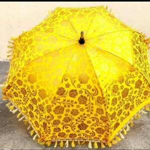 May include: A yellow umbrella with a floral pattern and gold fringe. The umbrella is made of fabric and has a wooden handle.