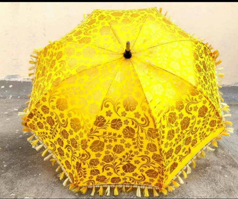 May include: A yellow umbrella with a floral pattern and gold fringe. The umbrella is made of fabric and has a wooden handle.