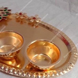 May include: A gold oval tray with two small bowls and a peacock design. The peacock is made of colorful enamel and has a blue head and green and red feathers. The tray is decorated with small red and gold flowers.