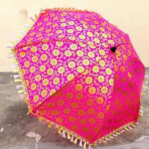 May include: A pink and gold umbrella with a floral pattern and tassels around the edge.