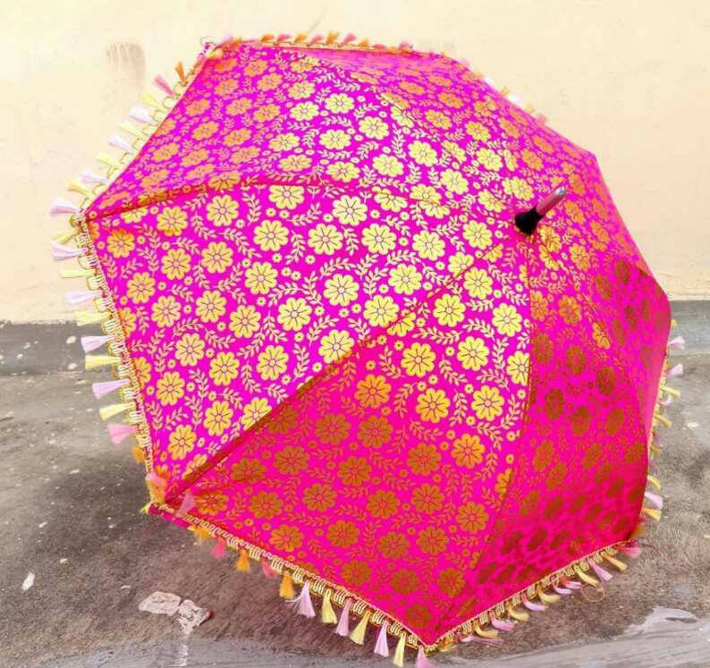May include: A pink and gold umbrella with a floral pattern and tassels around the edge.