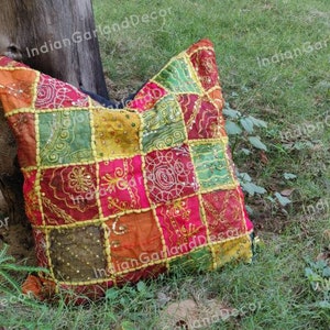 Könnte beinhalten: Ein farbenfrohes Patchwork-Kissen mit verschiedenen Stoffen und Stickereien. Das Kissen besteht aus einer Mischung aus roten, grünen, gelben, orangen und braunen Stoffen. Das Kissen liegt auf einem Bett aus grünem Gras.