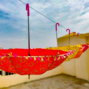 May include: A set of colorful umbrellas with pink handles and tassels hanging from a line. The umbrellas are red, yellow, and orange with floral patterns.