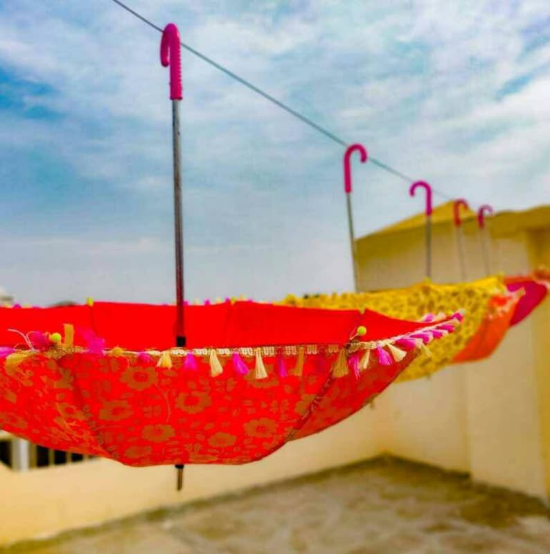 May include: A set of colorful umbrellas with pink handles and tassels hanging from a line. The umbrellas are red, yellow, and orange with floral patterns.