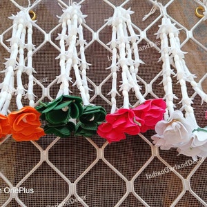 May include: Five strings of white artificial flowers with orange, green, pink, and white flower clusters at the bottom. The flowers are arranged in a row against a white wire mesh background.