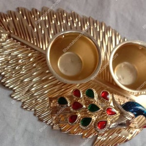 Puede incluir: Una bandeja de hoja de oro con dos cuencos pequeños y un diseño de pavo real. El pavo real tiene acentos azules, verdes y rojos.