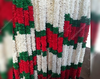 May include: A close-up of a garland made of white, red, and green paper flowers. The garland is arranged in a repeating pattern of white, red, and green. The garland is hanging from a wall and is decorated with the text "indiangarlanddecor".