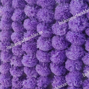 Peut inclure: Une guirlande de fleurs en papier violettes. La guirlande est composée de nombreuses petites fleurs duveteuses qui sont enfilées ensemble. Les fleurs sont de couleur violet clair et ont une texture douce et délicate.