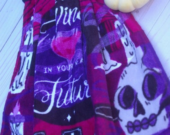 Peut inclure: Serviette de cuisine rouge et violette avec un crâne, des bougies et des bouteilles de vin imprimés dessus. Le texte "See your future in your tea" est imprimé sur la serviette.