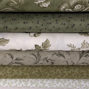 以下が含まれることがあります： さまざまな緑とクリーム色の生地のロールの山。生地には、大きな花、葉、繊細な小枝など、花柄と植物柄が施されています。キルトやその他の工芸品プロジェクトに適しています。